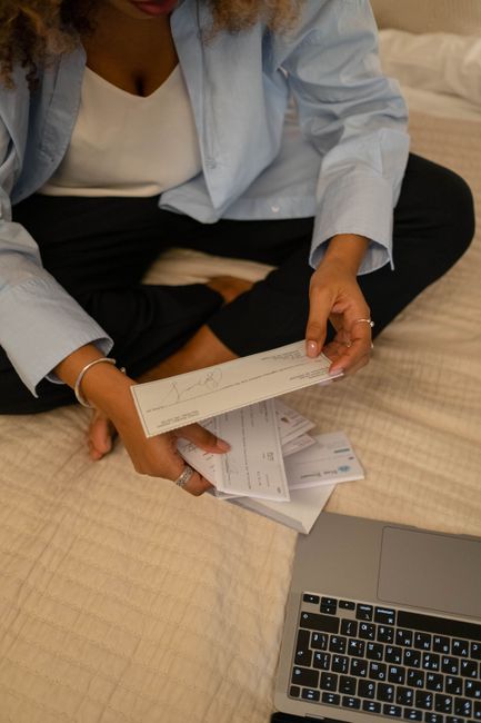 Individual sitting cross-legged examining papers near laptop