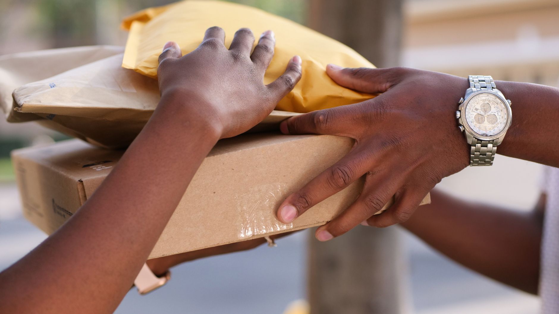 Two individuals exchanging cardboard and padded envelopes, r