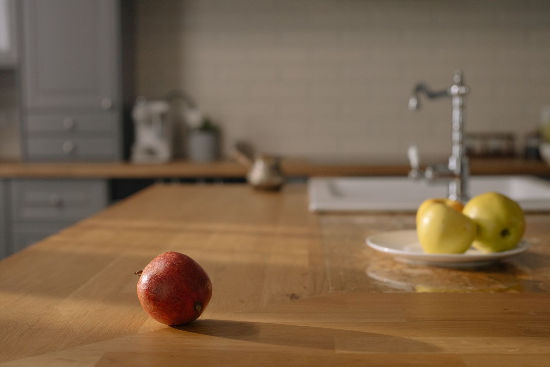 A red apple on a wooden counter and yellow apples on a plate