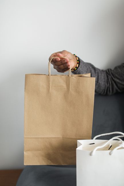 Close-up of a hand holding a brown paper shopping bag, empha