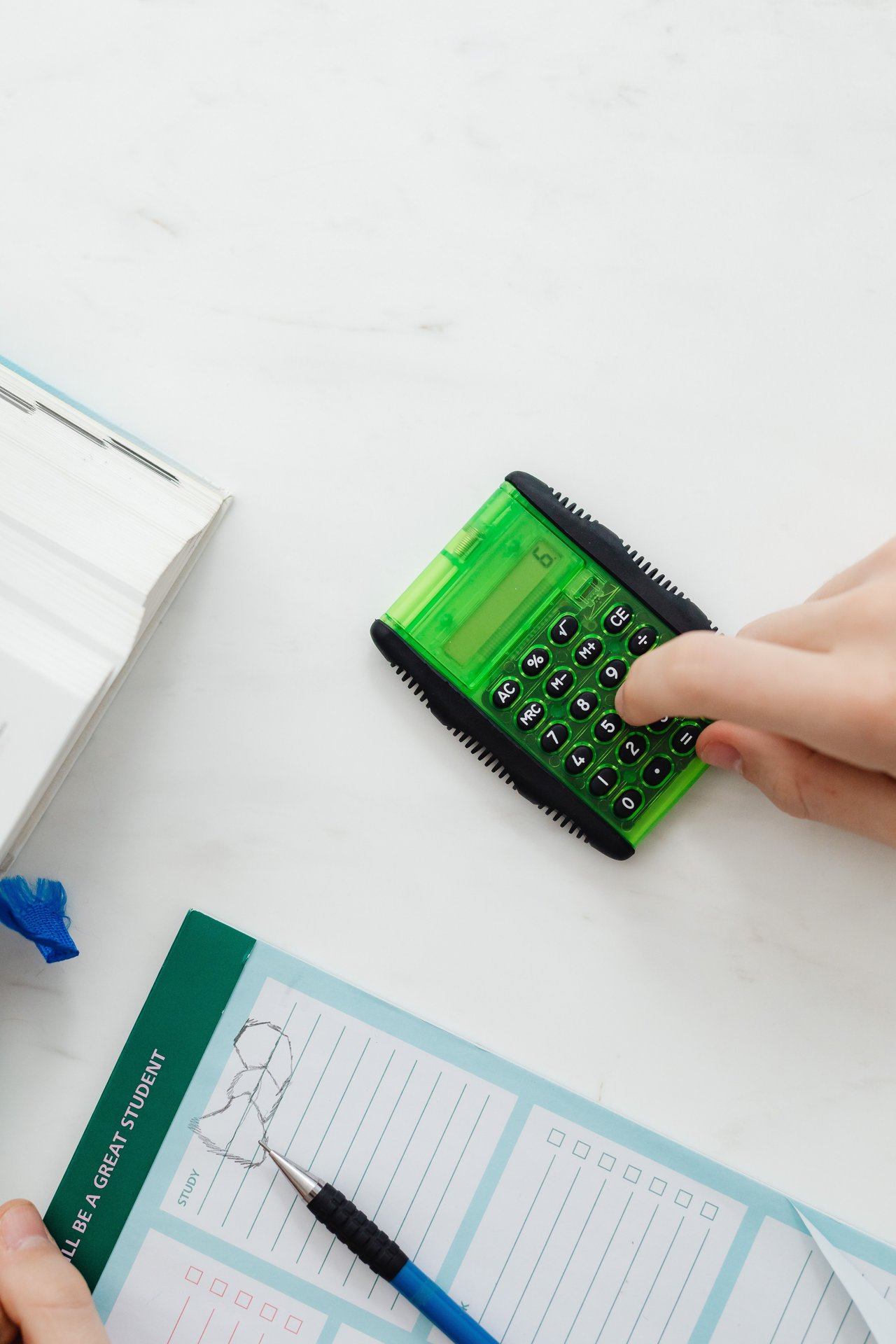 Close-up of hand using a green calculator on a study desk wi