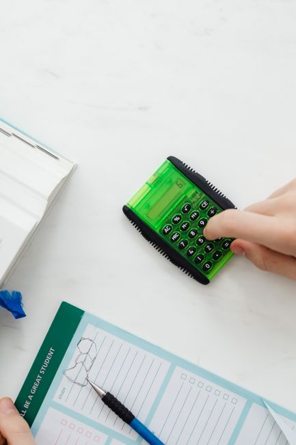 Close-up of hand using a green calculator on a study desk wi