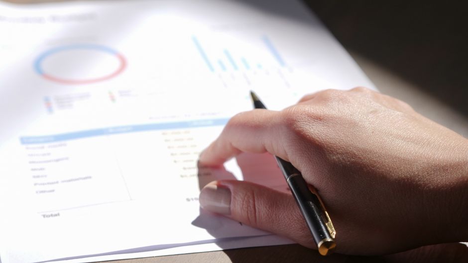 A close-up view of a hand holding a pen and examining financ