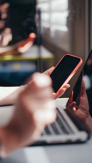 Hands holding smartphone near laptop, showcasing multitaskin