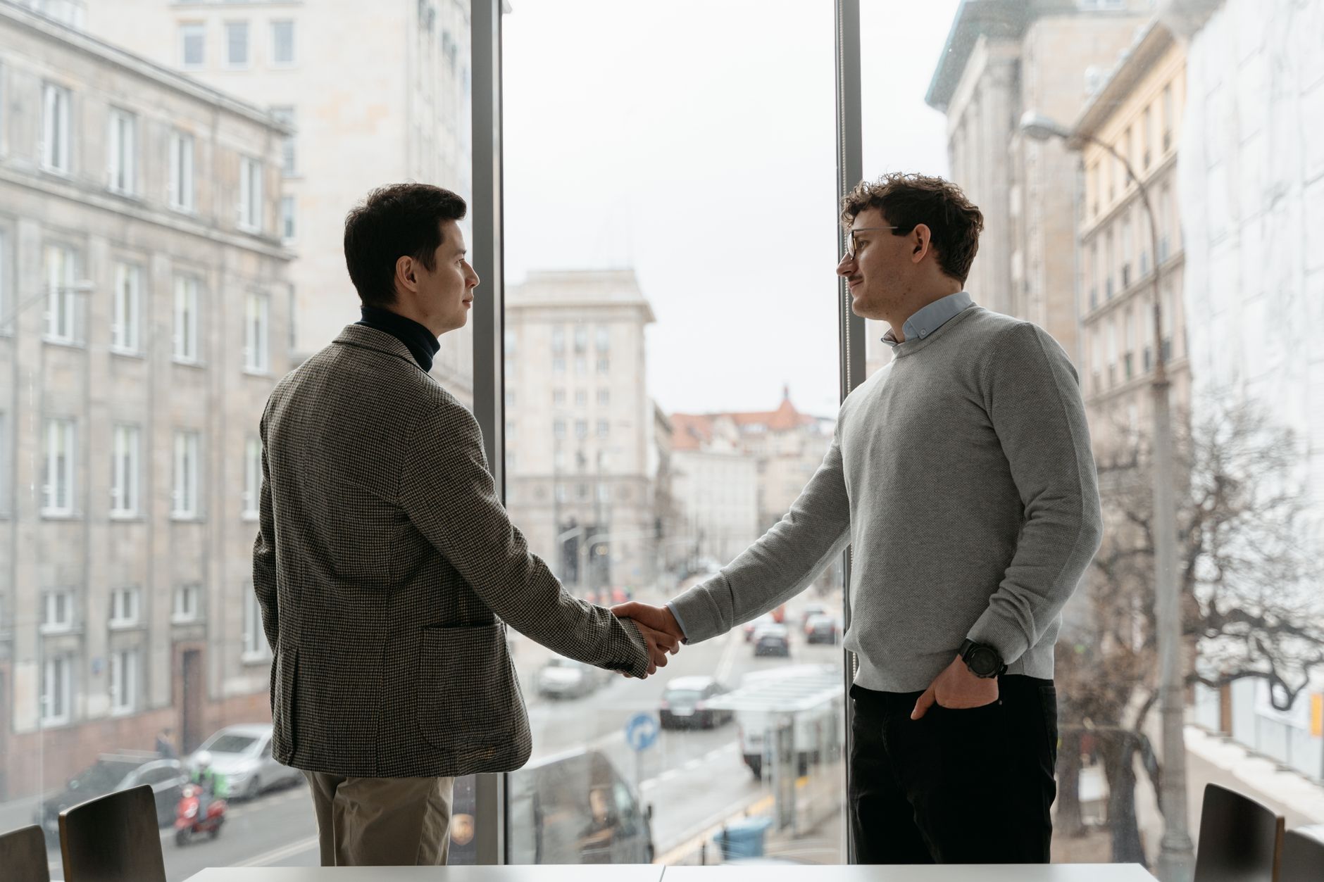 Two businessmen shaking hands in an urban office with city v