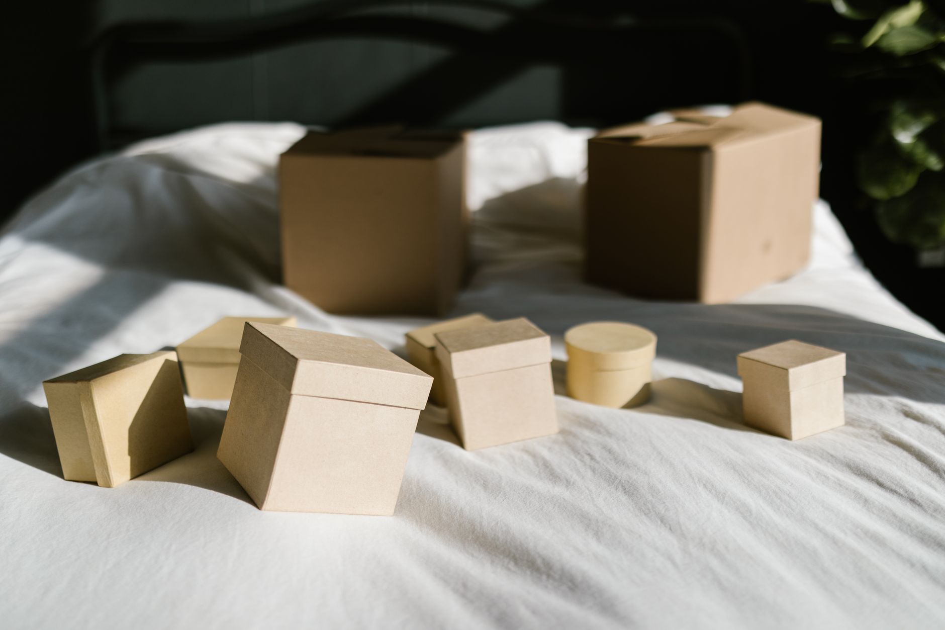 Cardboard boxes with lids arranged on a sunlit bed, casting