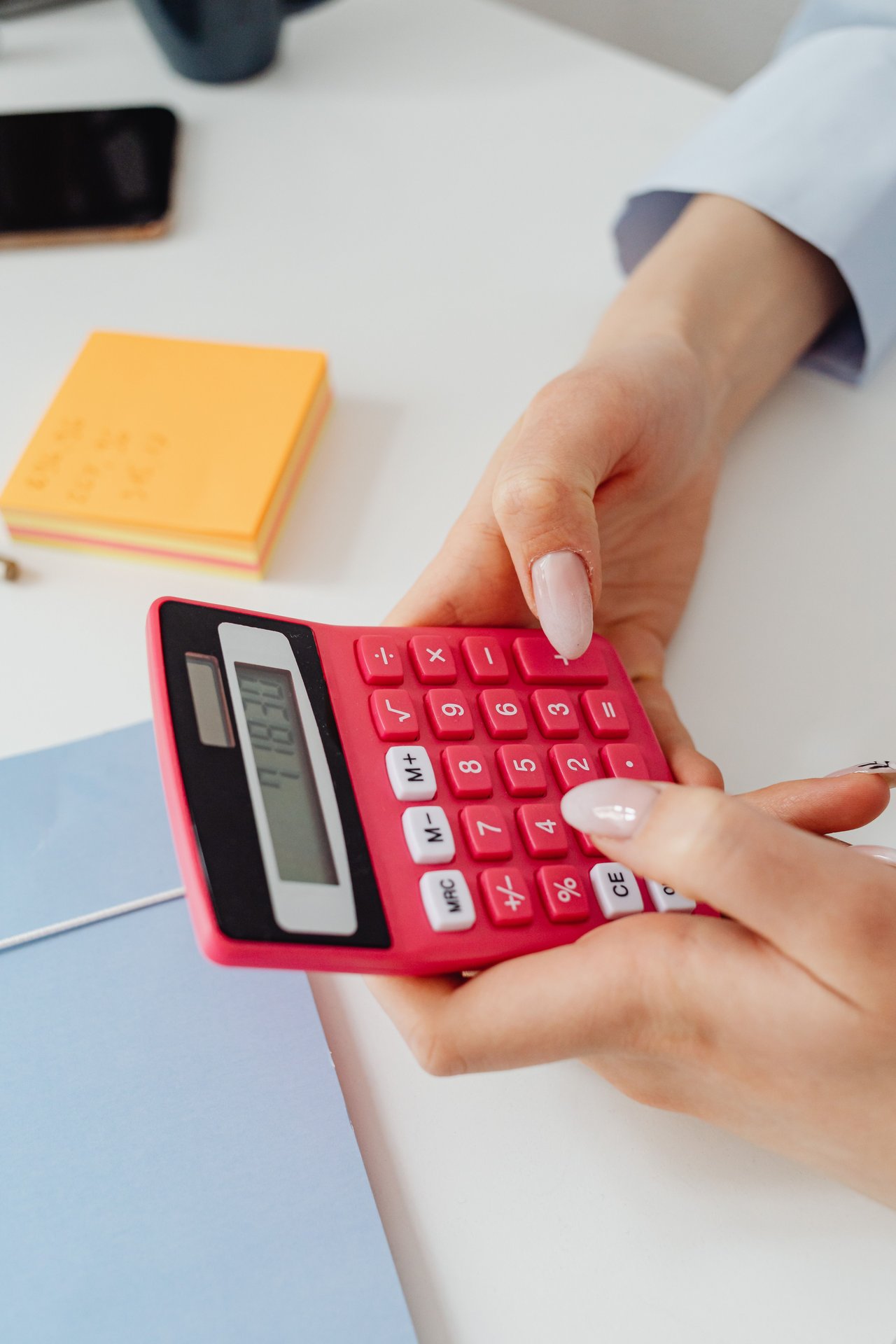 Detailed image of hands using a red calculator at a desk for