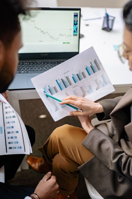 Two adults discuss financial data with charts and laptop in