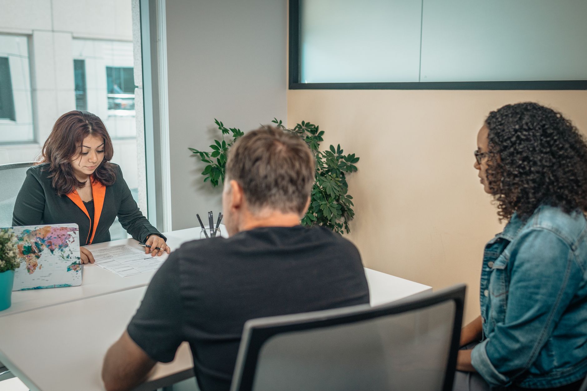 African American female worker speaking with unrecognizable diverse clients at desk with paper sheet and laptop in modern workspace