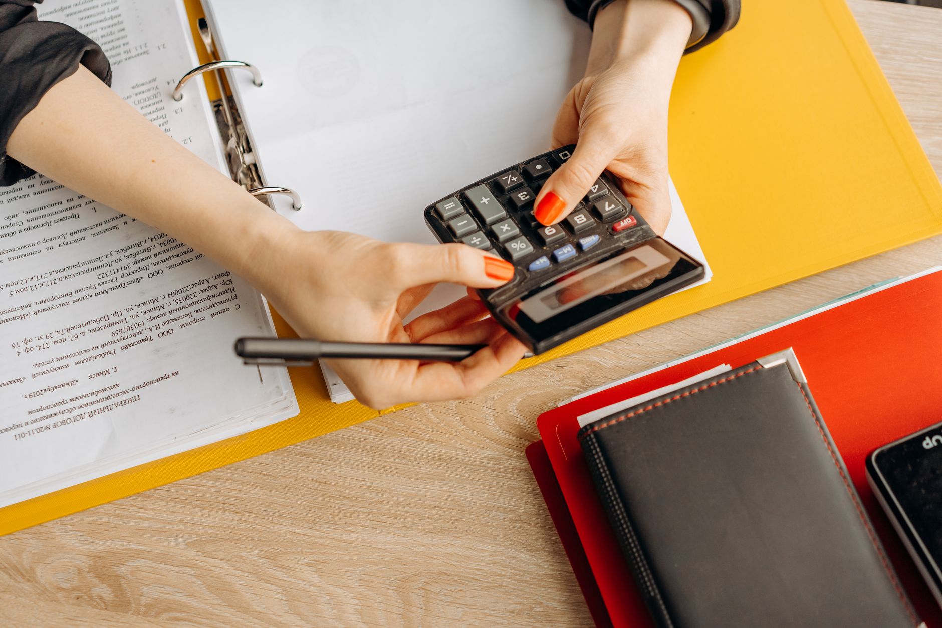 Hands using a calculator at a desk with documents and folder