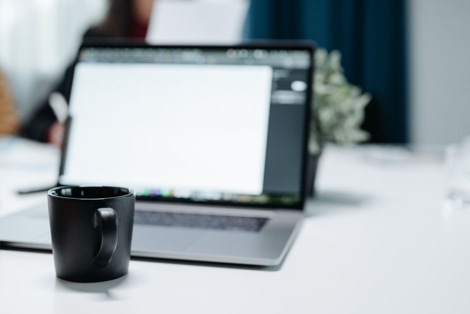 A black coffee mug on an office desk with a blurred laptop i
