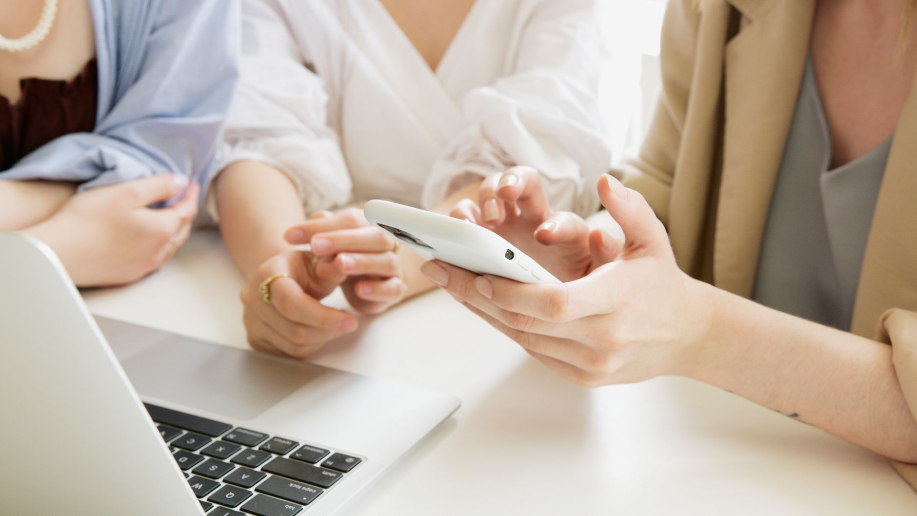 Three women collaborate using a smartphone and laptop in a p