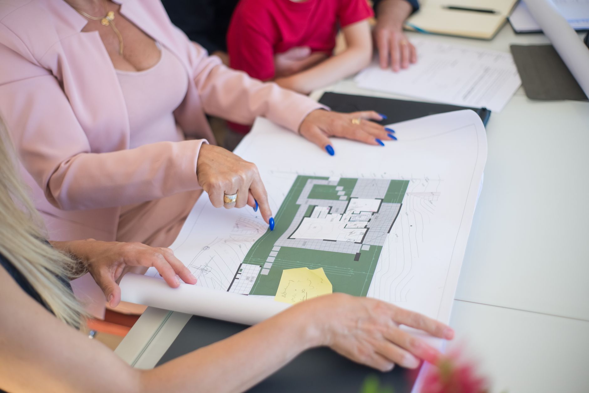 A real estate agent in a pink blazer shows floor plans to cl