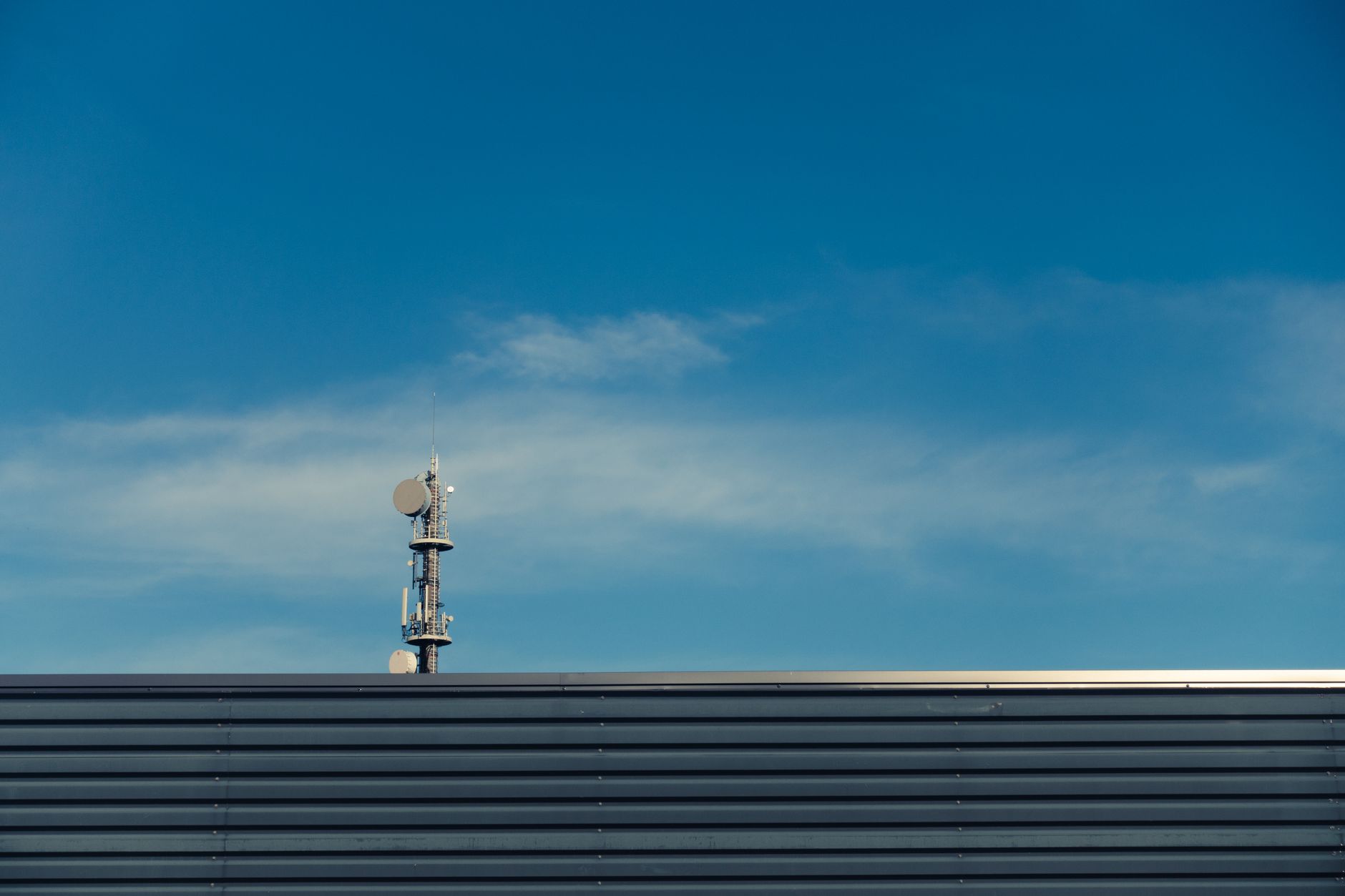 A modern telecommunication tower stands against a clear blue