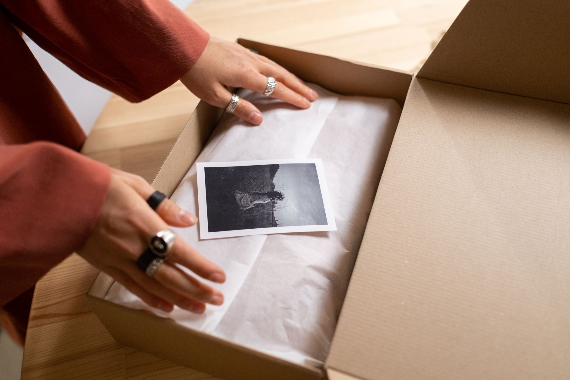 Hands opening a cardboard box revealing a photograph wrapped