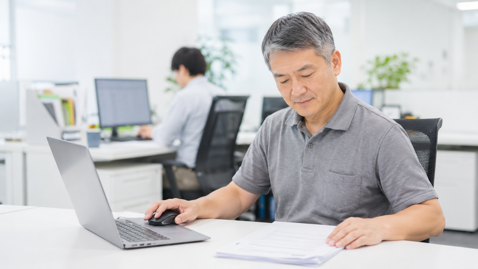 オフィスの自席で納品書とノートパソコンを見比べる日本人の会社員