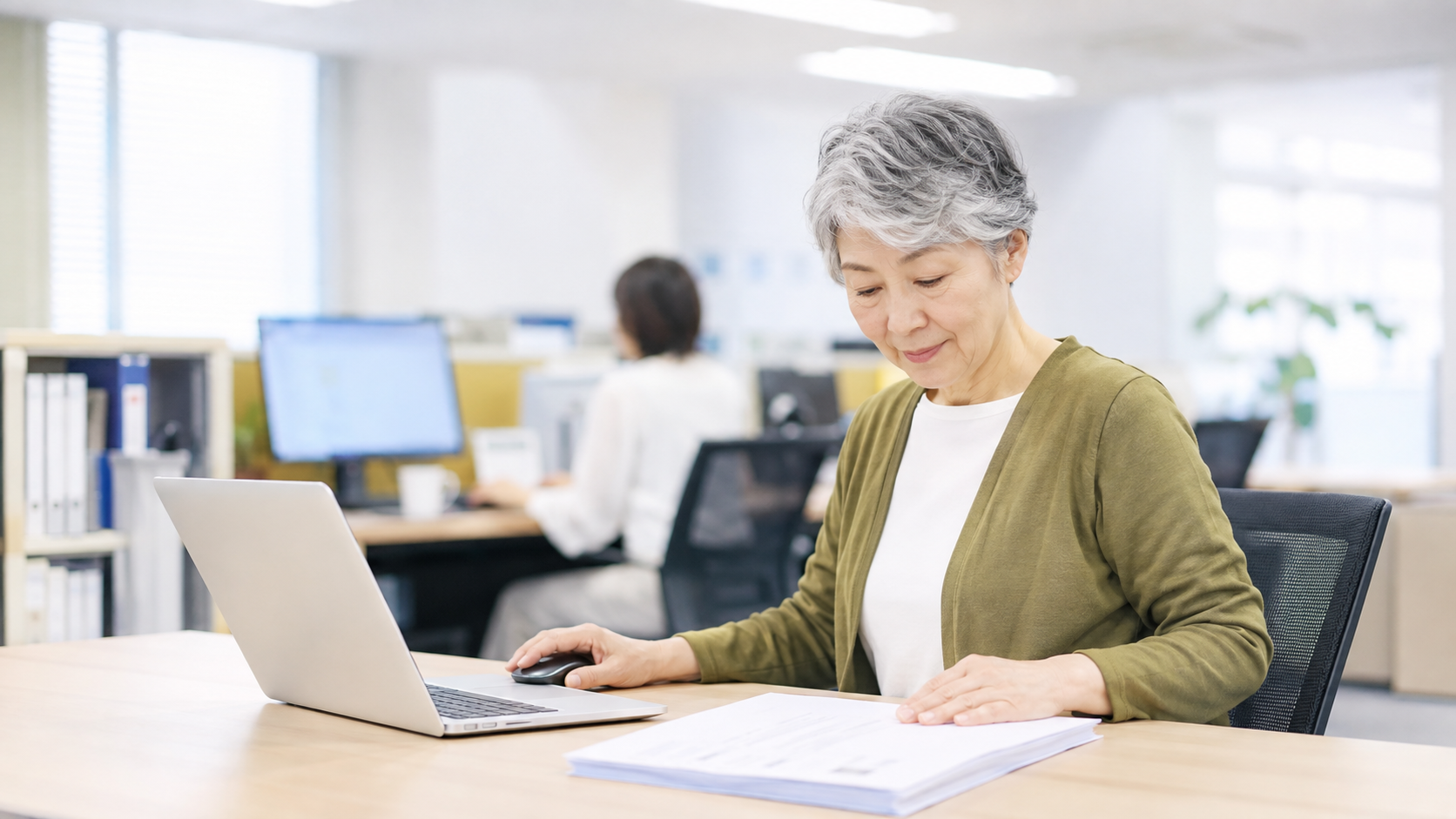 オフィスの自席で納品書とノートパソコンを見比べる日本人の会社員