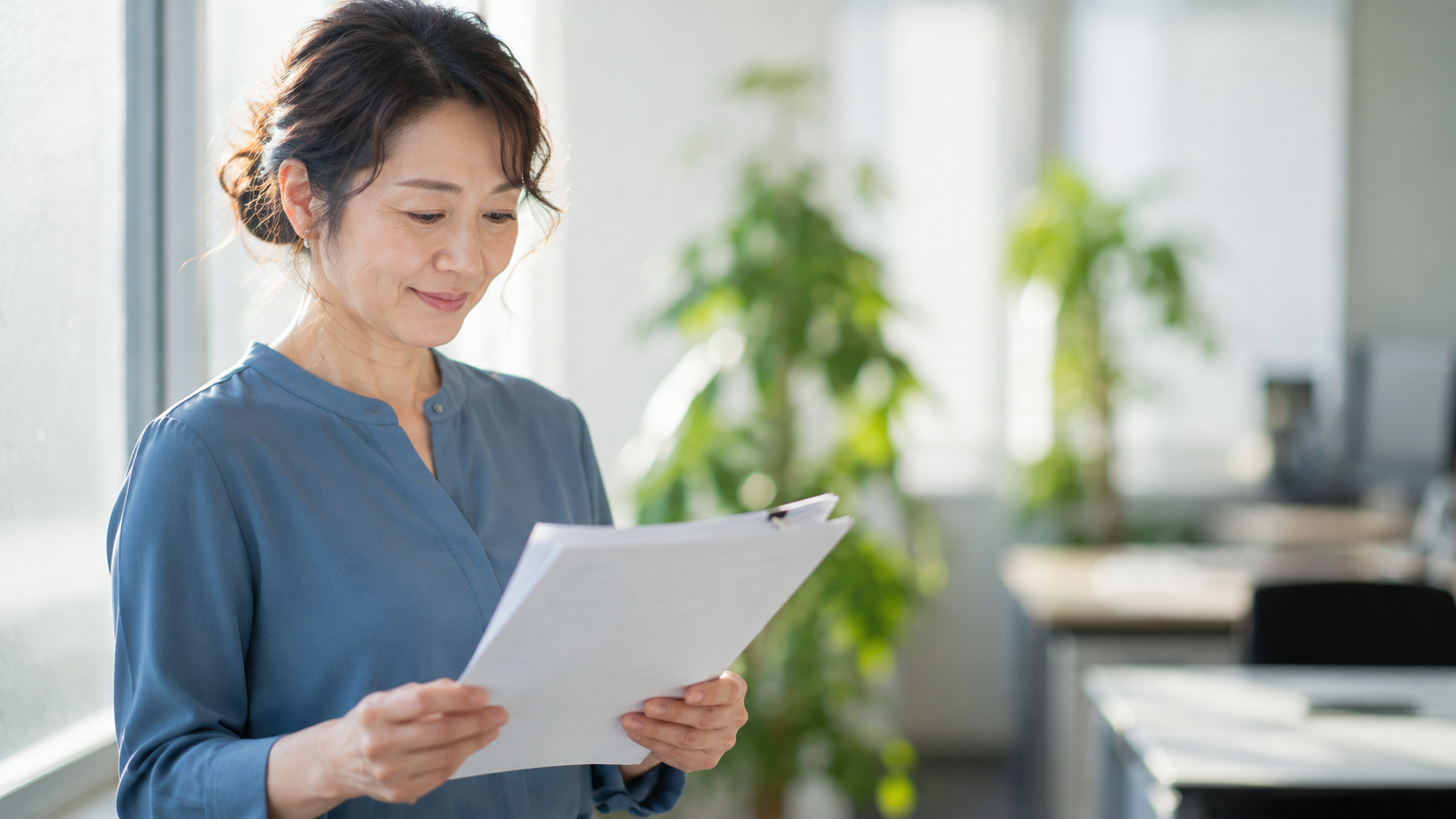 50代前半の日本人女性が窓際での書類確認場面