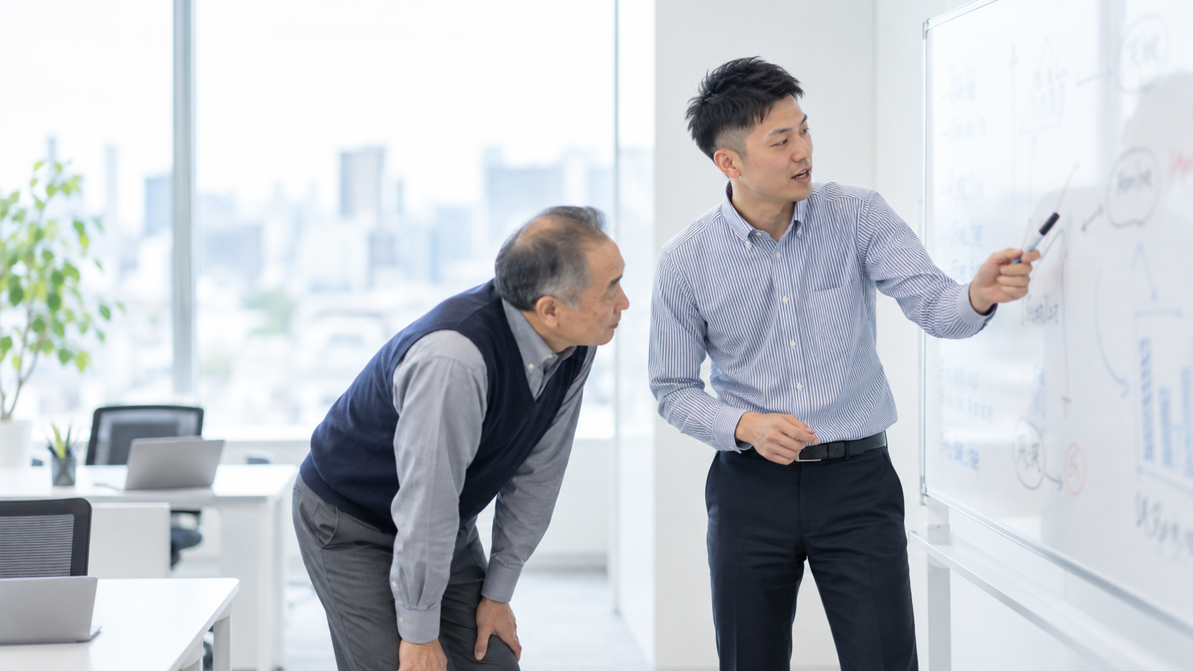 20代後半の日本人男性がホワイトボードでの説明をしている場面