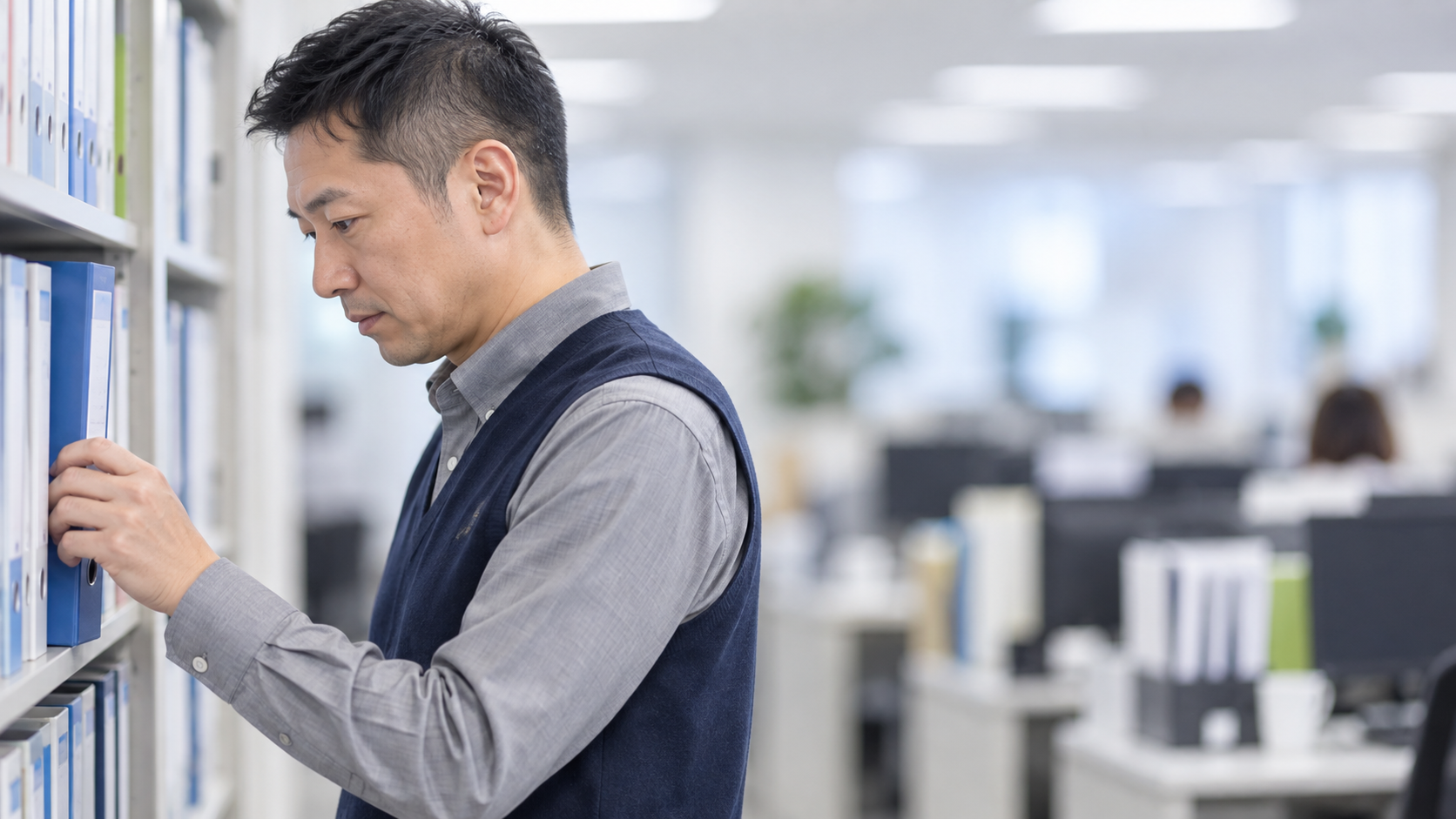 40代前半の日本人男性が書庫でのファイル探しをしている場面