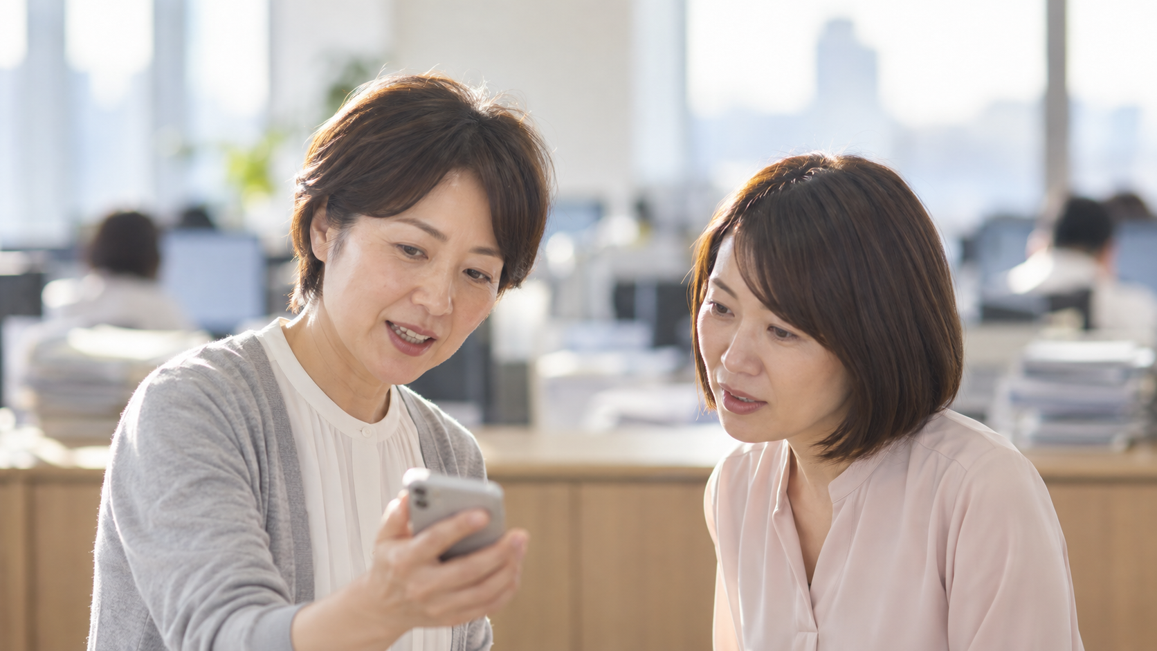 40代後半の日本人女性がスマートフォンの画面提示をしている場面