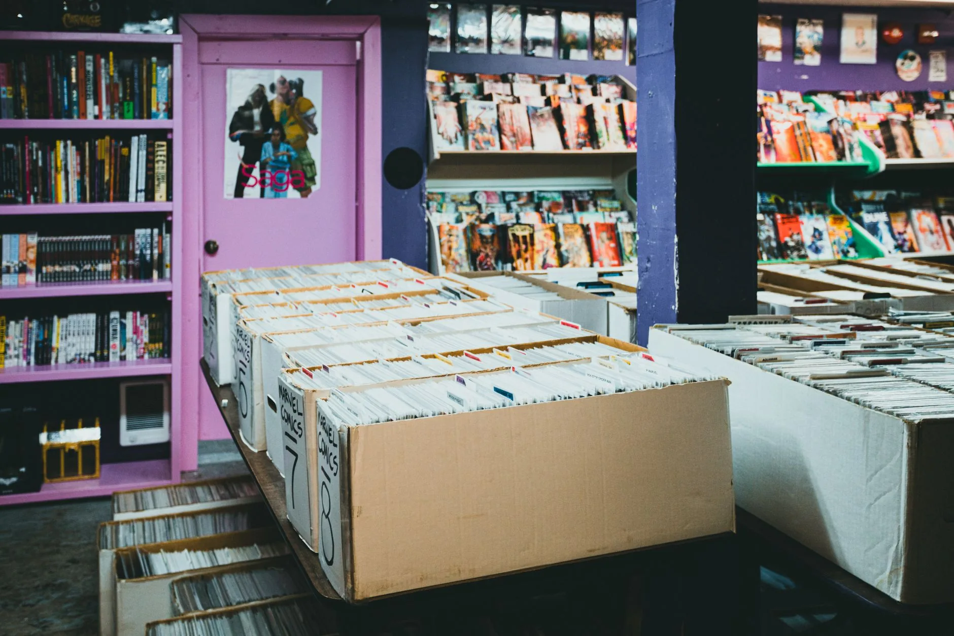 A colorful comic book store with organized shelves and boxes of comics for sale.