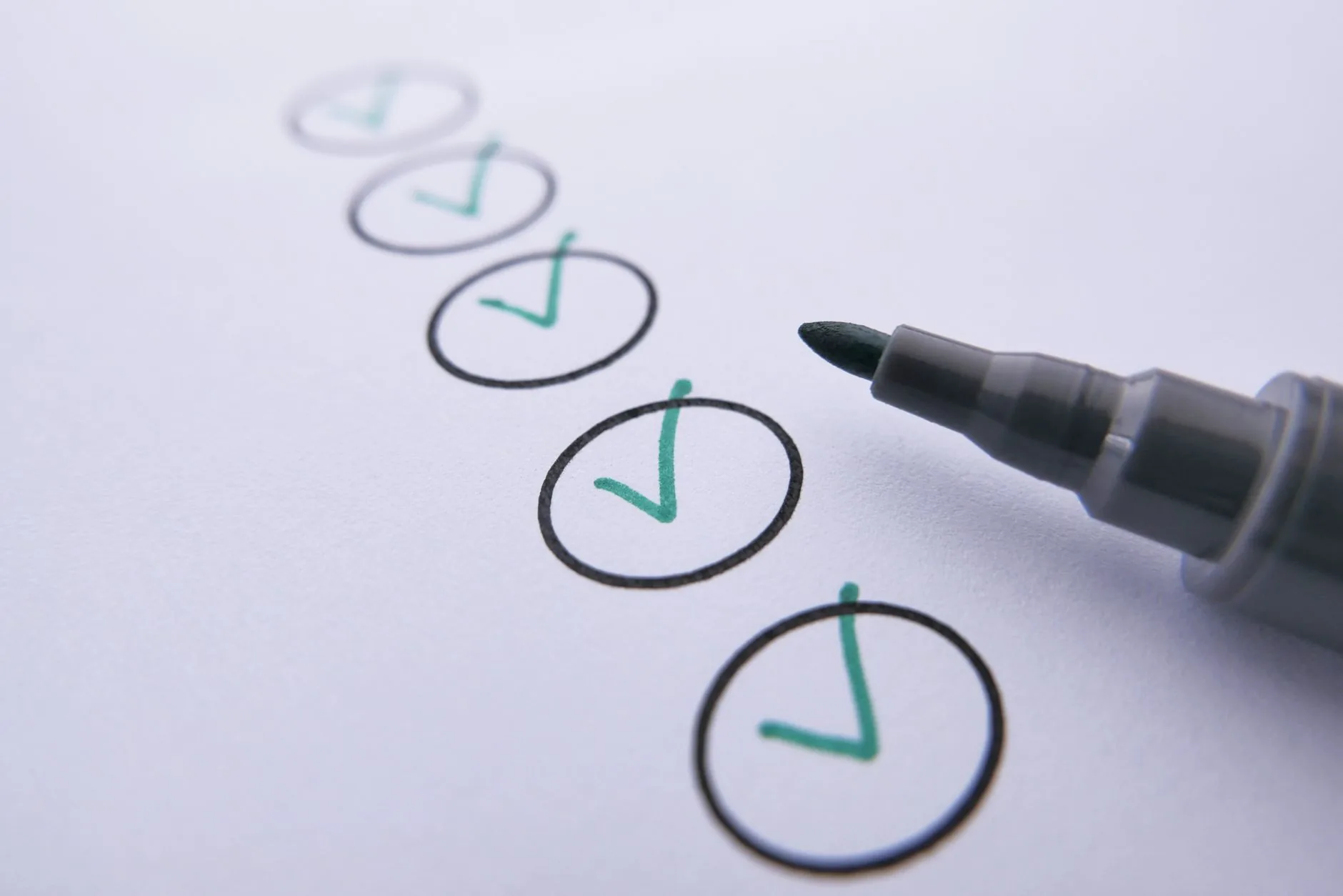 Close-up of a checklist with green checkmarks on white paper using a marker.