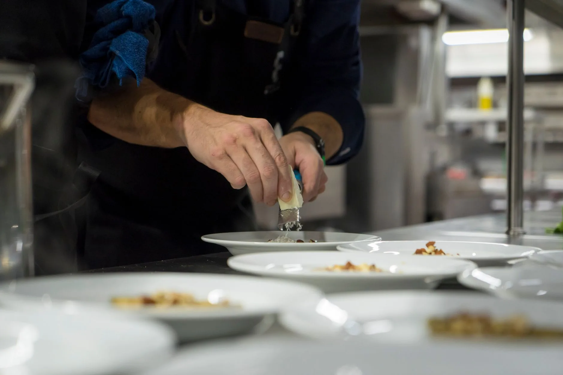 A chef grates parmesan over beautifully arranged plates in a high-end restaurant kitchen.