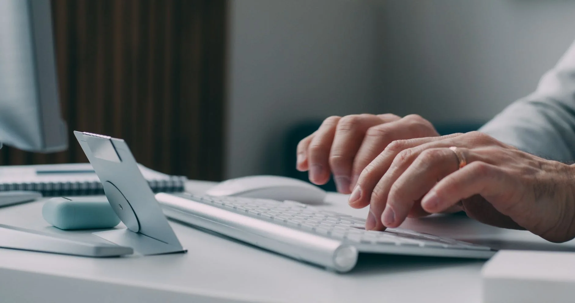 Hands typing on a keyboard at a modern workspace, close-up view.