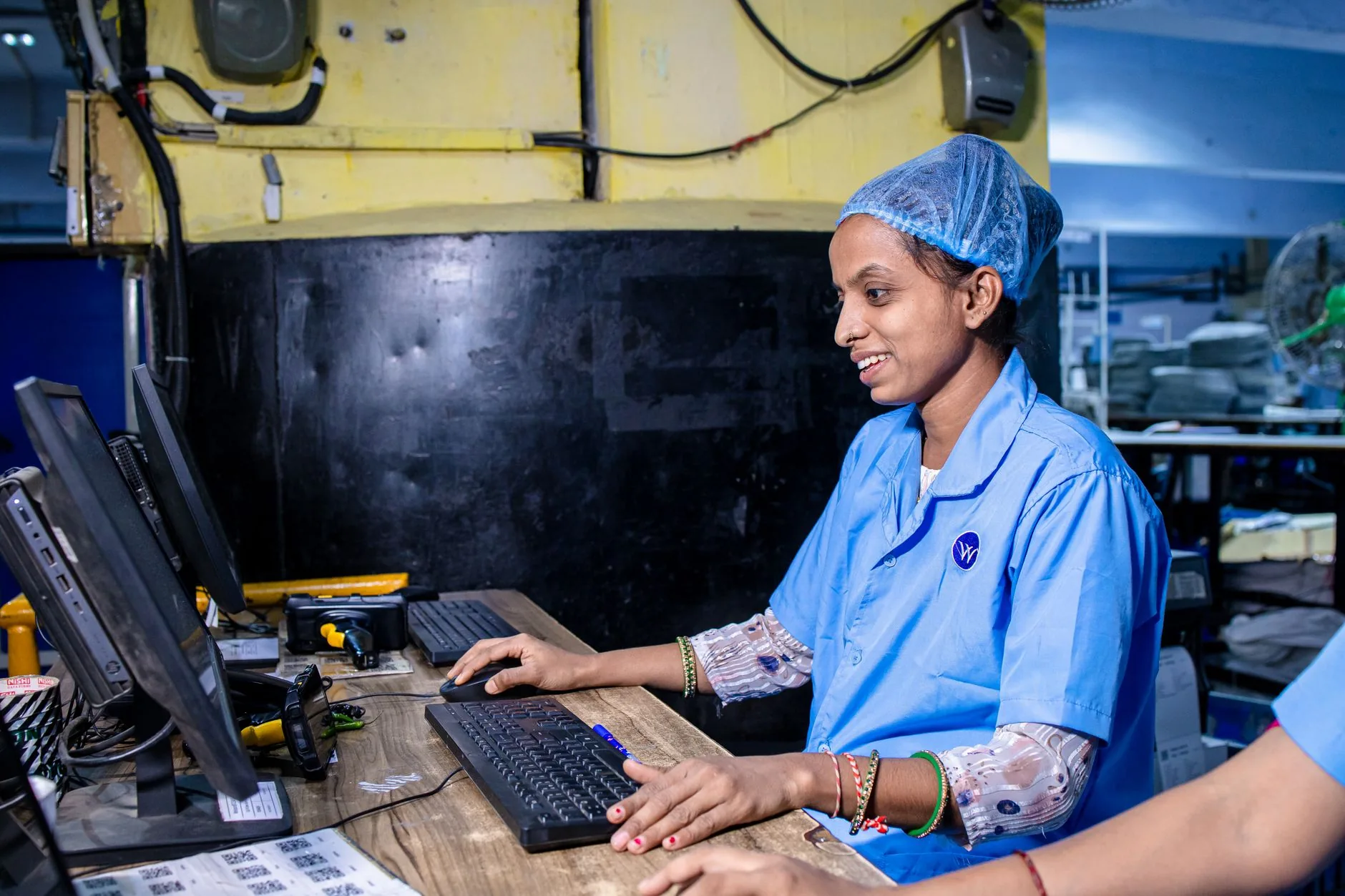 Female factory worker in blue uniform operating a computer in a textile factory.