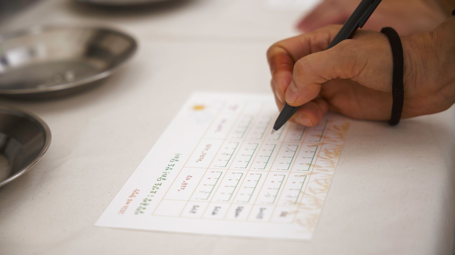 Detailed view of a hand writing on a form with a pen at a table.