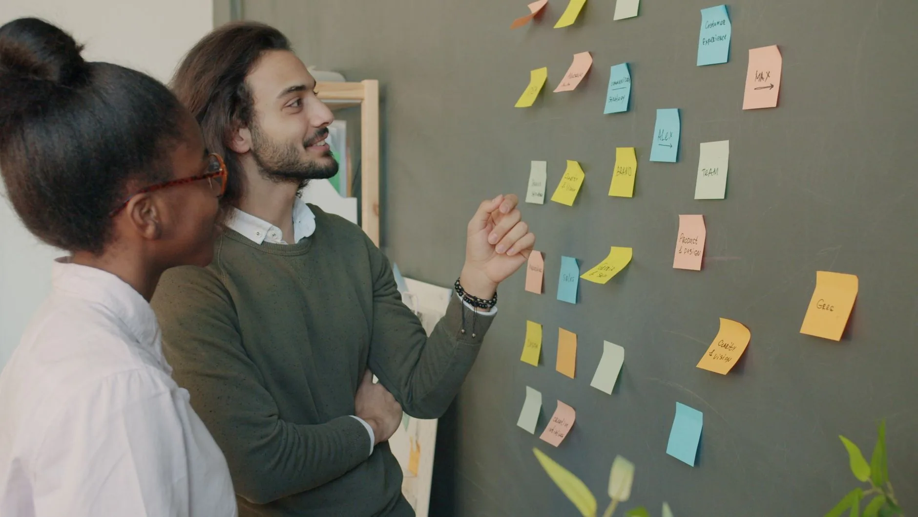 Two colleagues brainstorming ideas on a blackboard with colorful sticky notes.