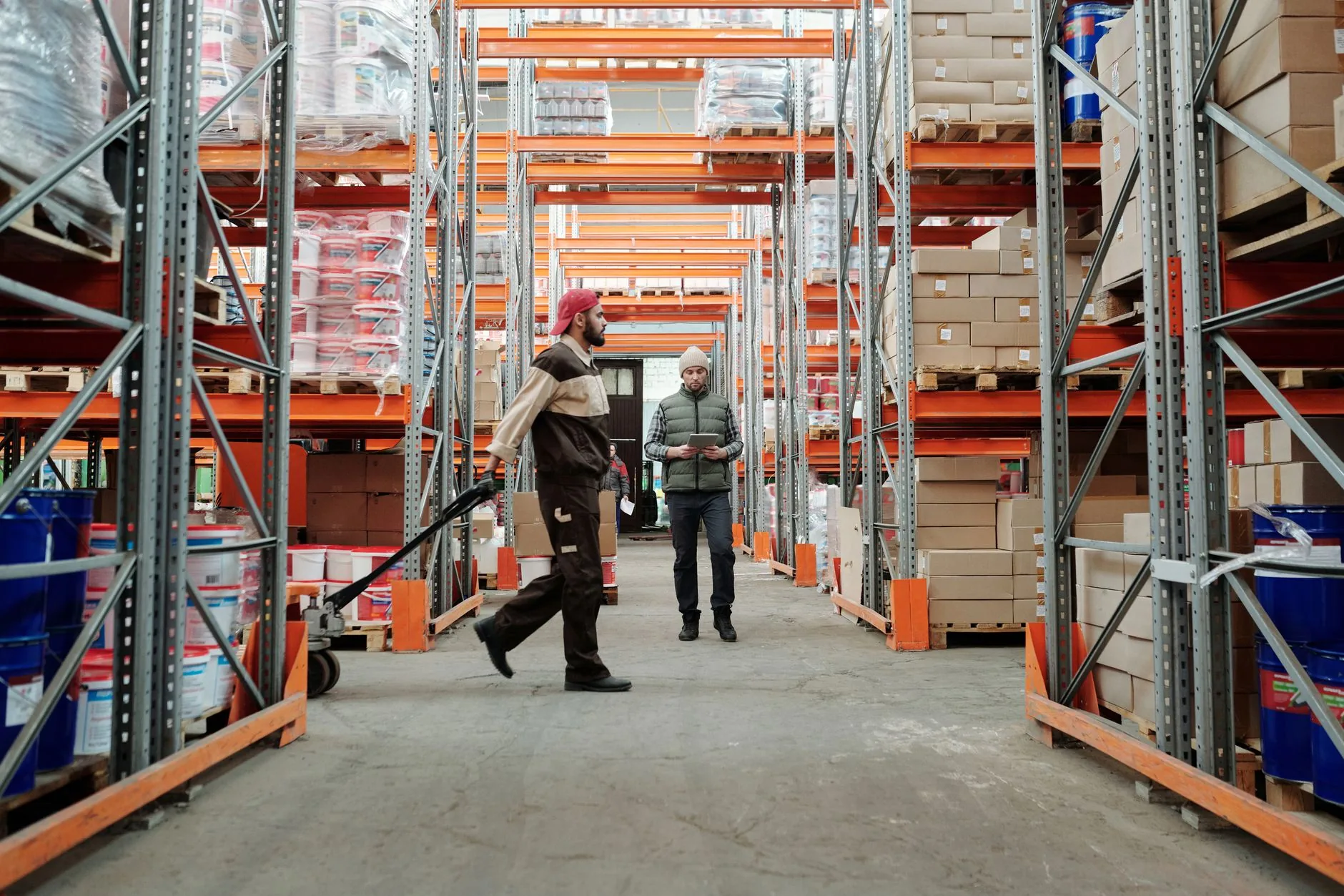 Two workers manage inventory in a spacious warehouse aisle.