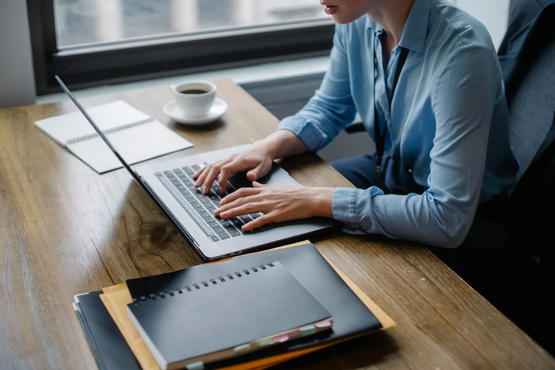 Office worker typing on laptop with coffee and notebooks on desk, capturing a focused work setting.