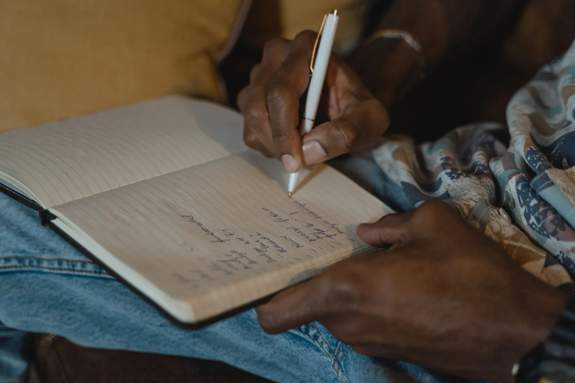 A detailed close-up of hand writing notes in a lined notebook using a white pen indoors.