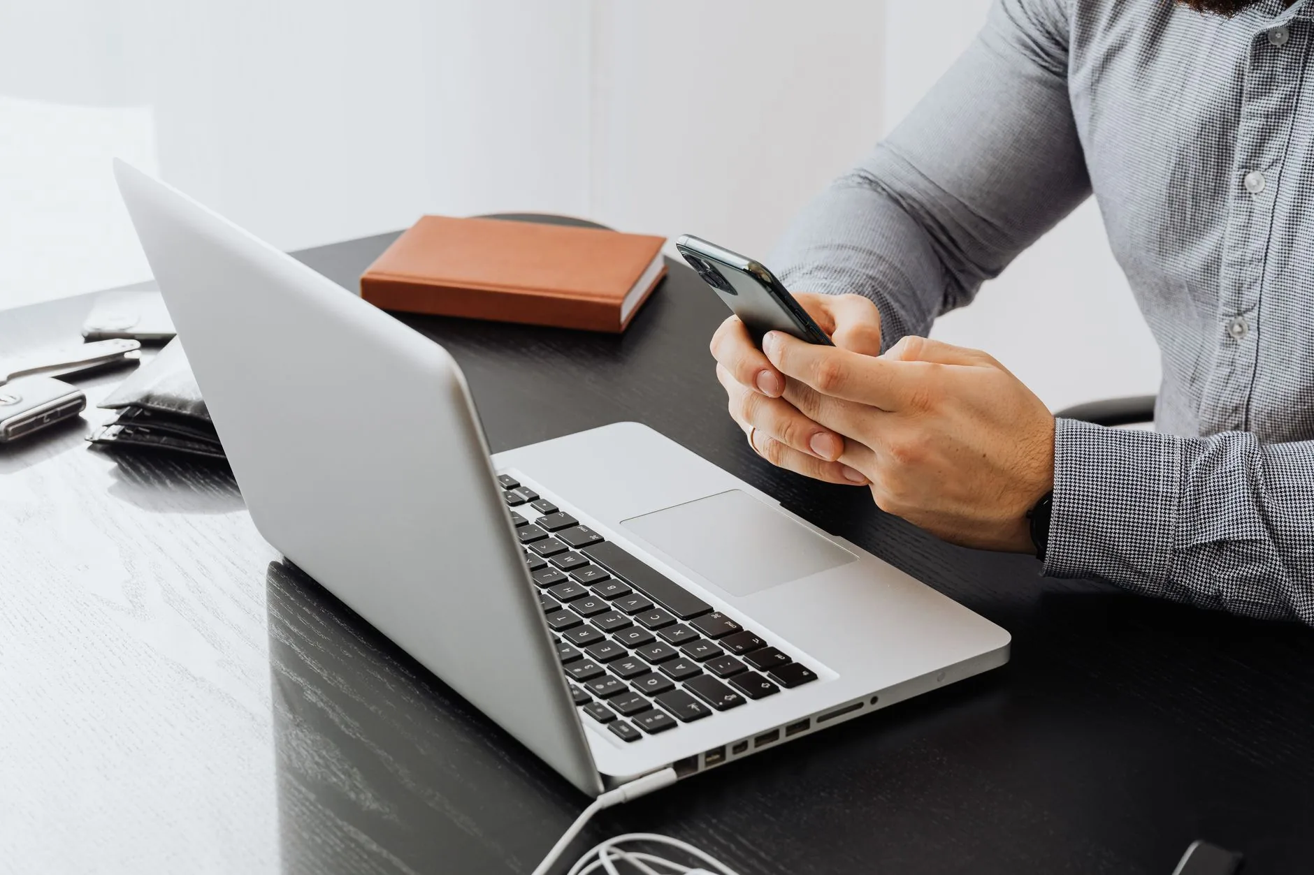 An adult using a smartphone at an office desk with a laptop for work.