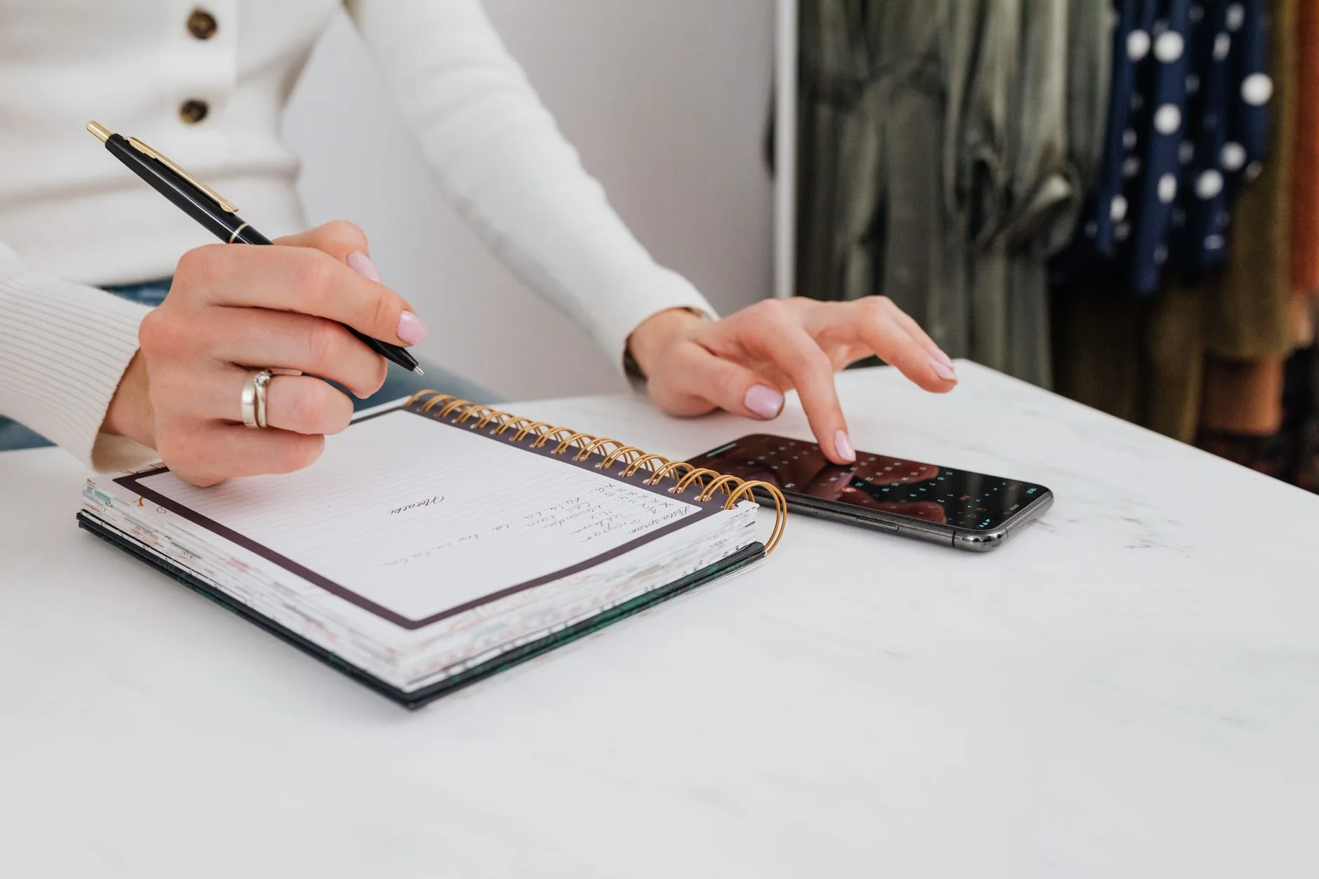 Close-up of hands writing in a notebook, with a smartphone on the table.