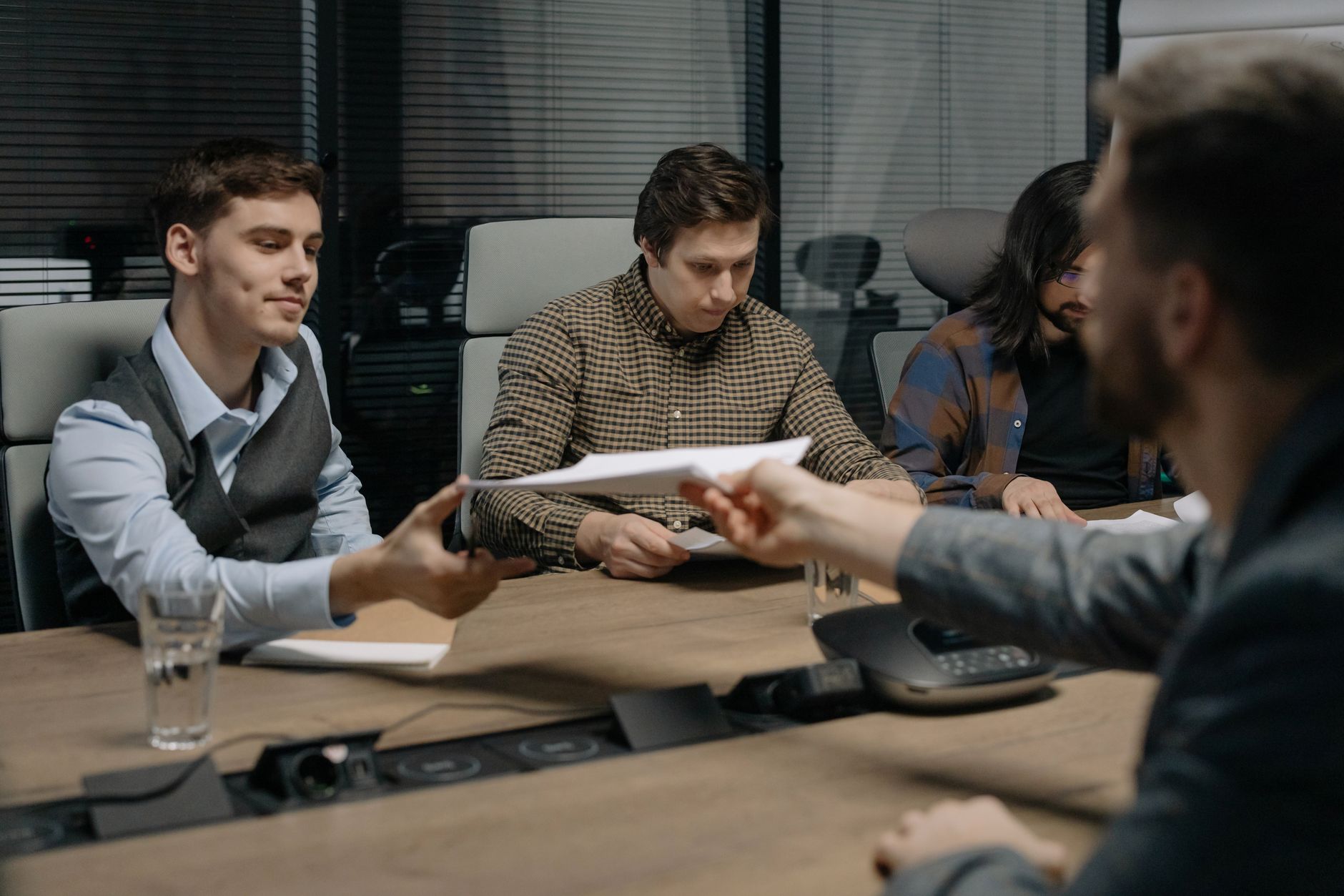 Four professionals exchanging documents during a meeting in an office setting.