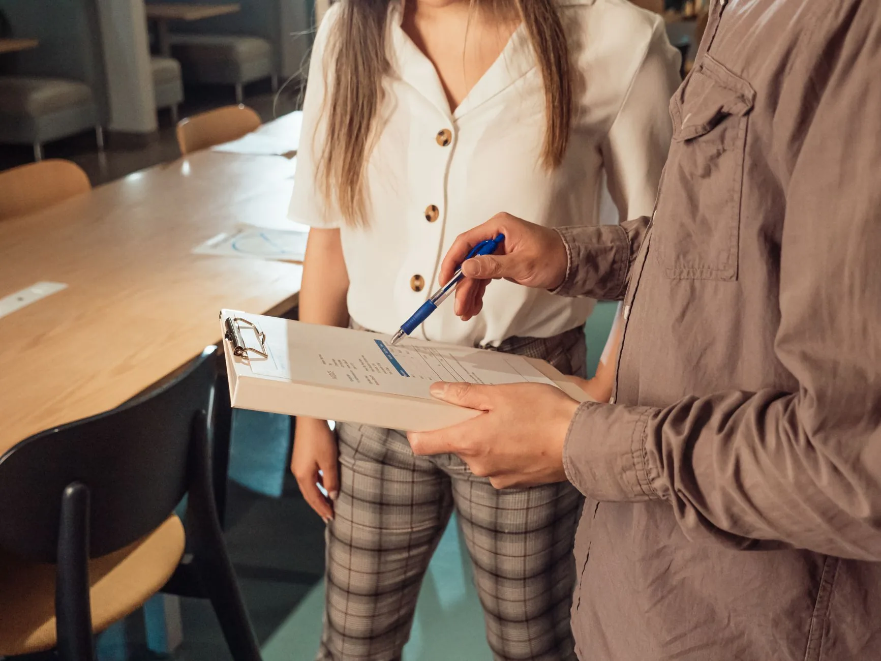 Two adults in a business setting discussing documents on a clipboard.