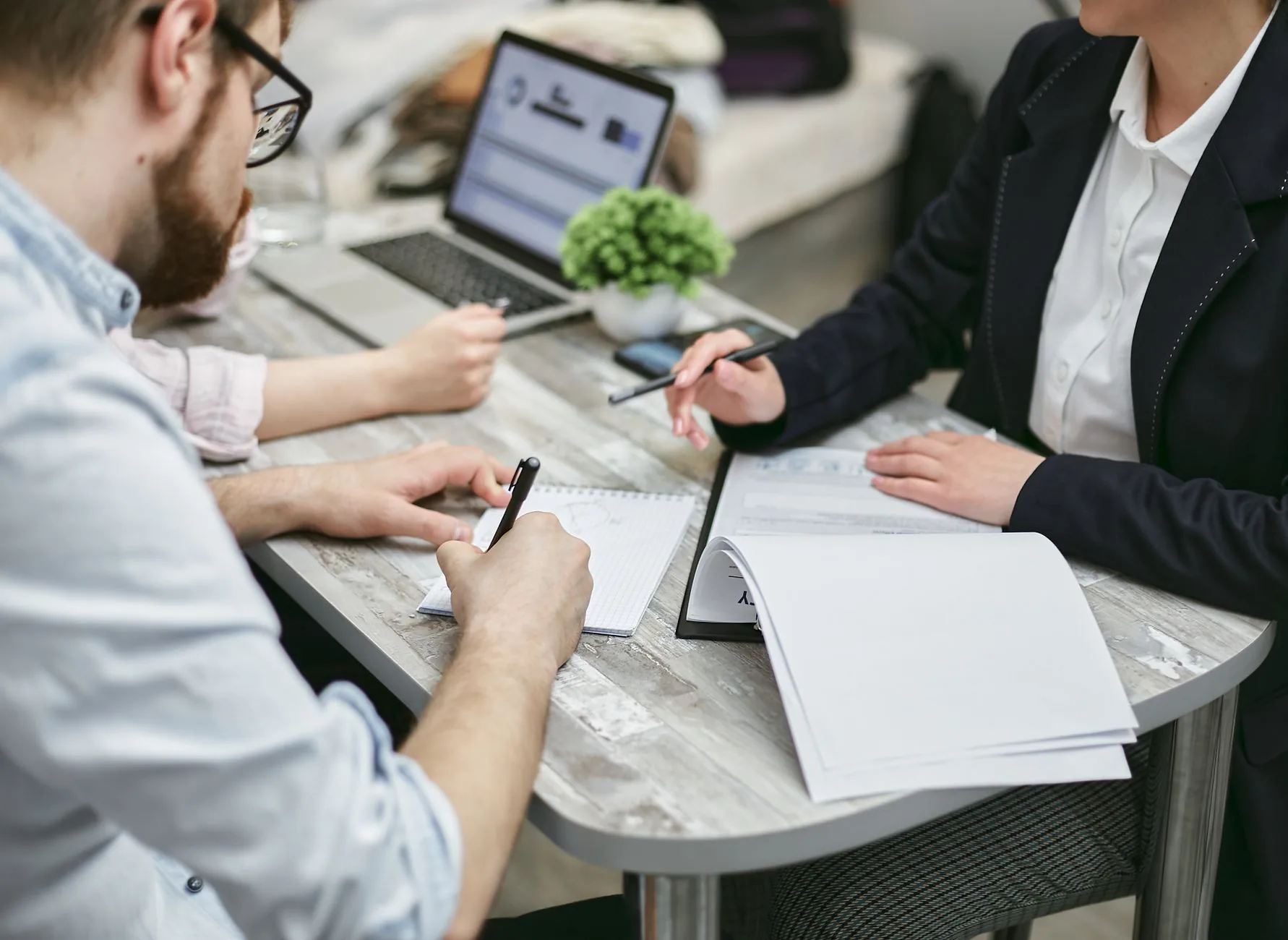 Colleagues collaborating and taking notes at a desk, discussing business documents.