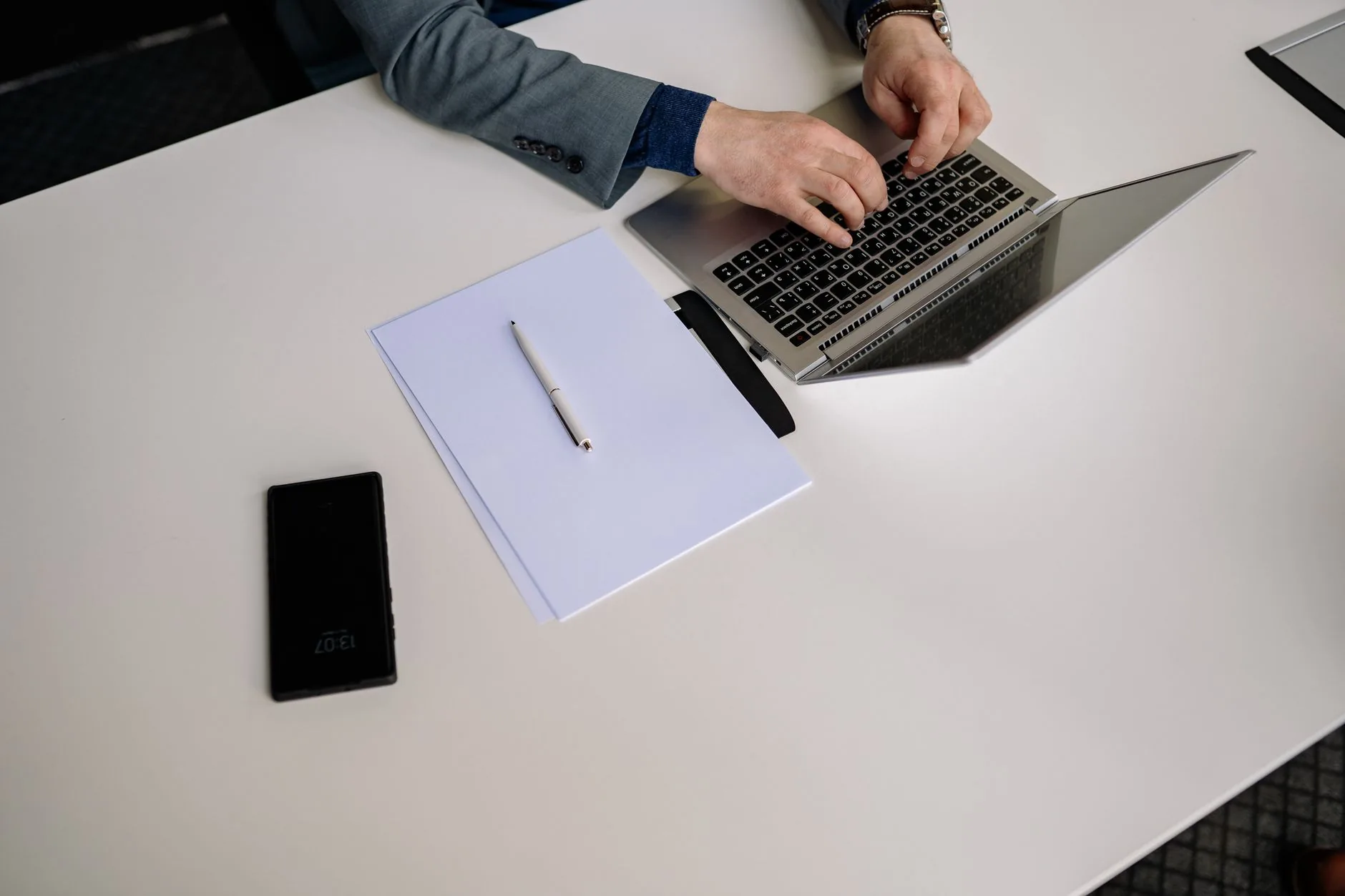 Top view of businessman typing on a laptop at a neat white desk with phone and papers.