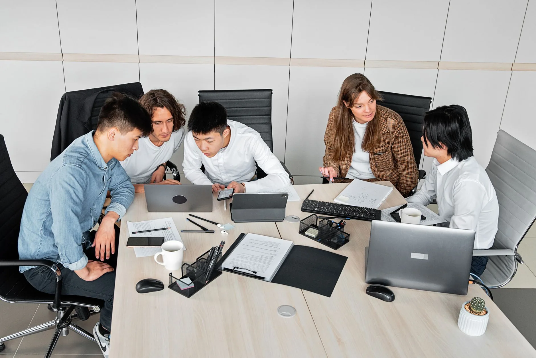 A diverse group of colleagues working together in an office setting with laptops and documents.