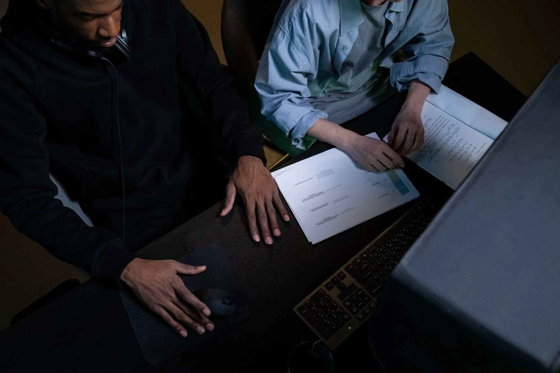 Two colleagues work over papers and a computer at a desk, collaborating effectively.