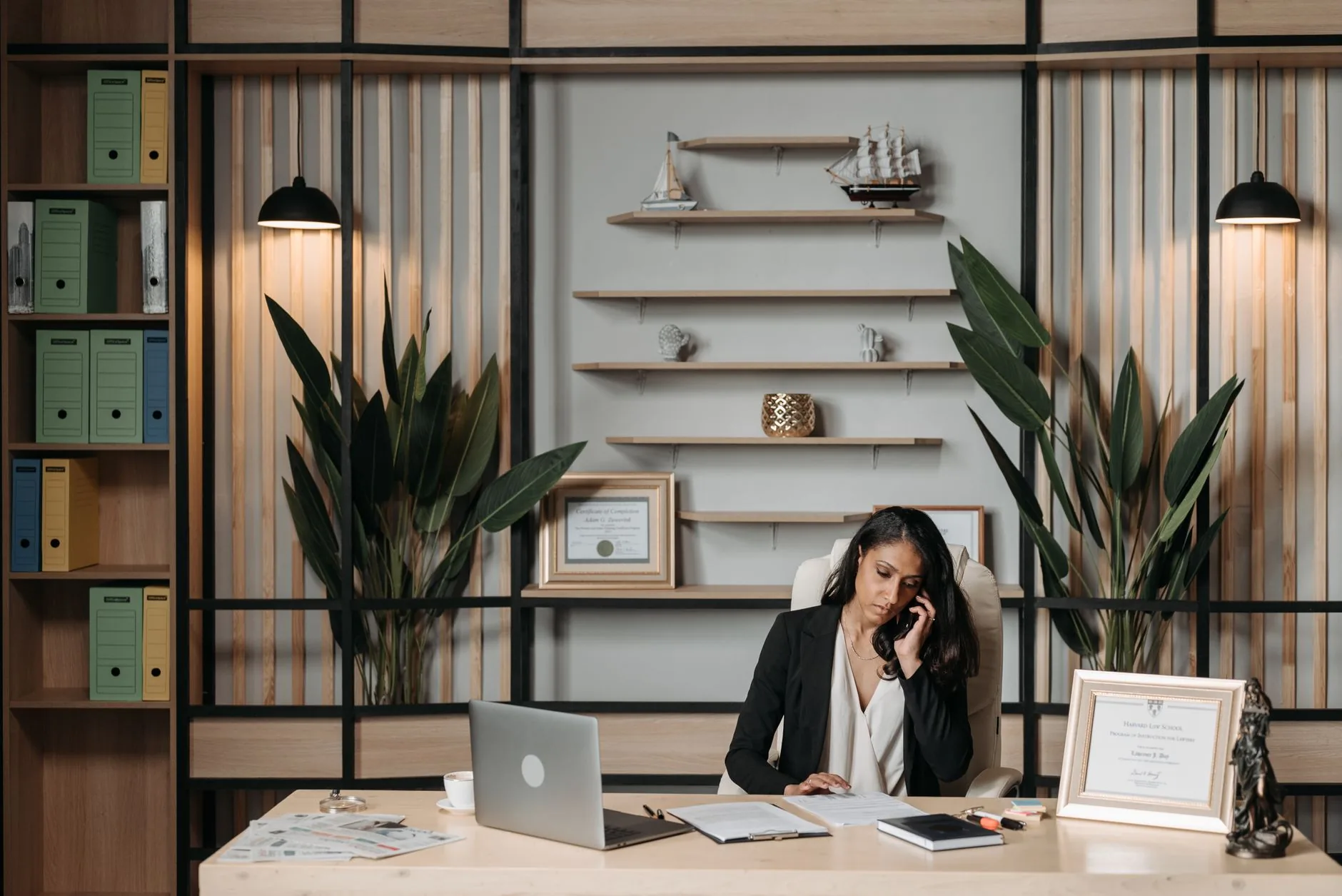 Businesswoman at desk in a stylish office, engaged in phone conversation with paperwork.