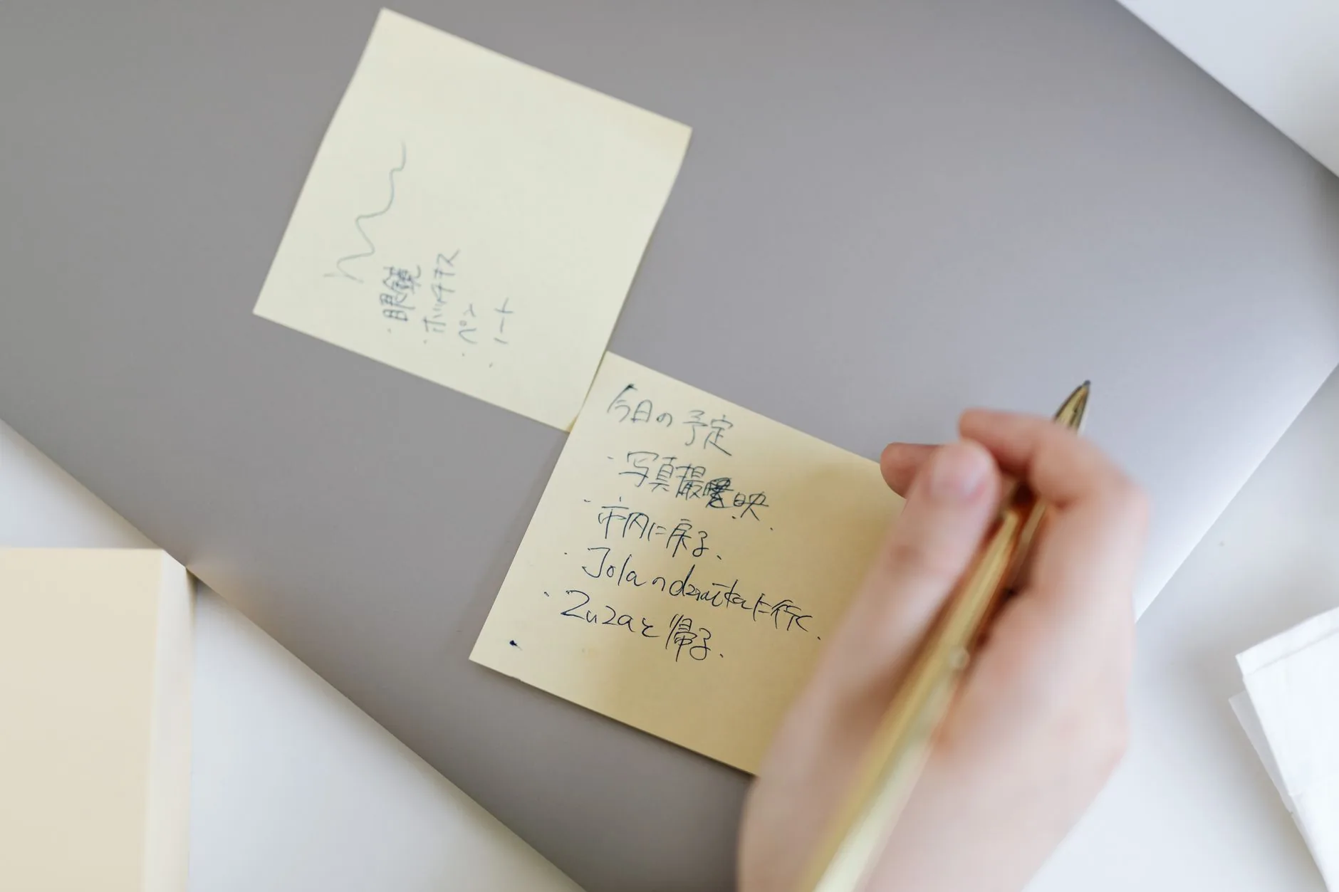 Close-up of a hand writing notes on sticky notes placed on a laptop, emphasizing planning and organization.