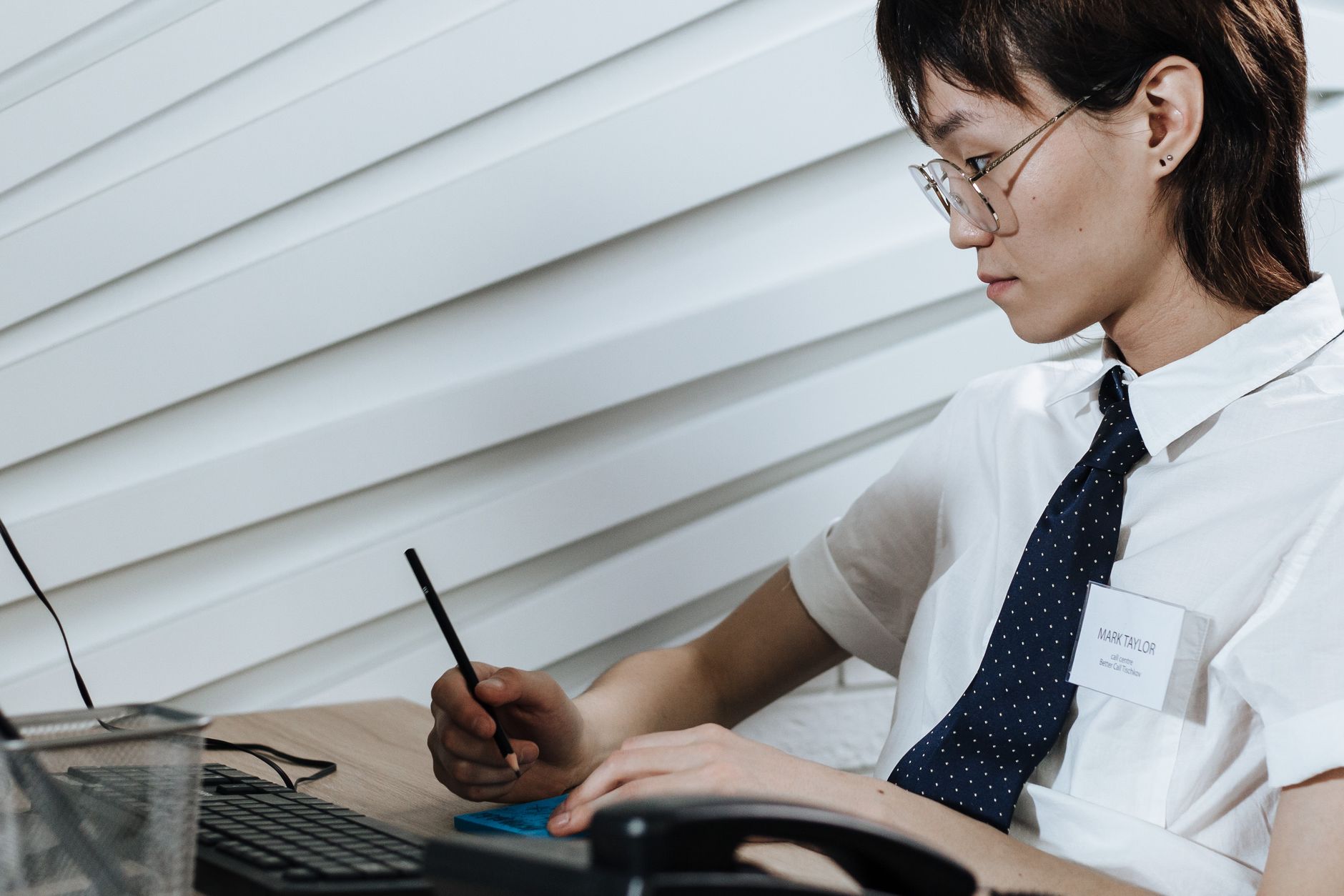 Office worker in eyeglasses taking notes at desk with computer in modern setting.