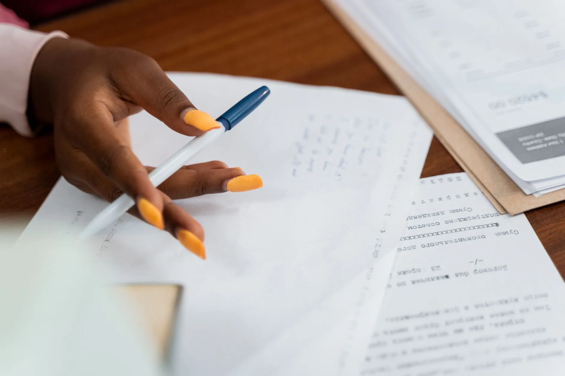 A hand over paperwork at a desk, with pen and writing notes, suggests a busy working environment.