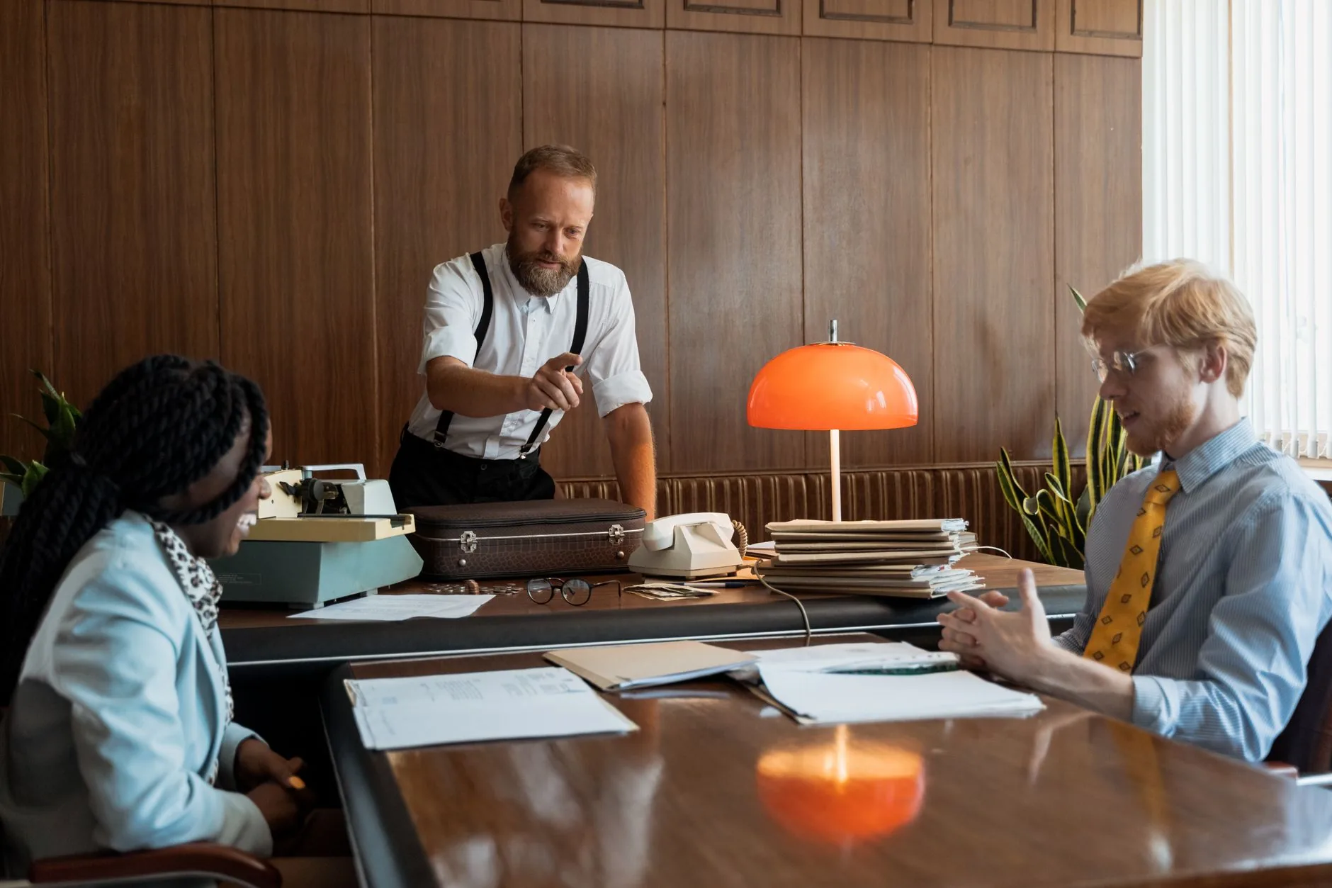 A vintage office meeting with three adults discussing documents around a table.