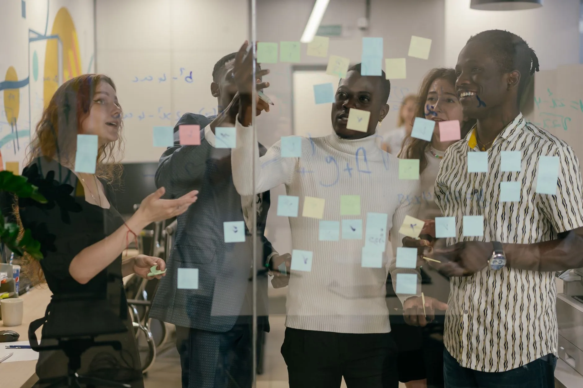A diverse group of colleagues collaborates using sticky notes on a glass wall in an office.