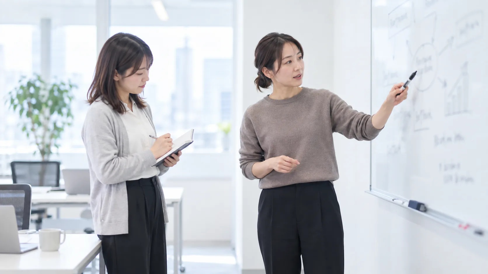30代後半の日本人女性がホワイトボードでの説明をしている場面